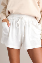 These white shorts feature a high waisted design, an elastic waistband, a self-tie drawstring, functional front pockets, and a wide leg.