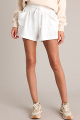 Front view of these white linen shorts that feature a high waisted design, an elastic waistband, a self-tie drawstring, functional front pockets, and a wide leg.