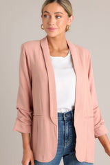 Close up front view of this dusty rose blazer featuring a folded neckline, shoulder padding, faux pockets, and gathering in the quarter-length sleeves.