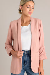 Close up angled view of this dusty rose blazer featuring a folded neckline, shoulder padding, faux pockets, and gathering in the quarter-length sleeves.