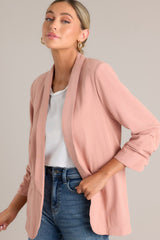 A dusty rose blazer featuring a folded neckline, shoulder padding, faux pockets, and gathering in the quarter-length sleeves.