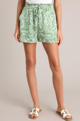 Front view of these green tropical print shorts that feature a high waisted design, an elastic ruffled waistband, a self-tie drawstring, functional hip pockets, and a wide leg.