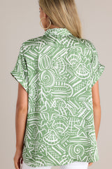 Back view of this green tropical print top that features a collared neckline, a functional button front, wide folded short sleeves, and a split hemline.