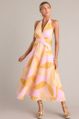Angled full body view of this light pink & orange dress  features a self-tie halter neckline, open back, thick waistband, discrete back zipper, and flowing silhouette.