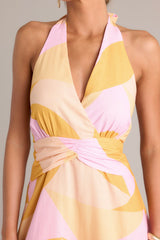 Close up view of this light pink & orange features a self-tie halter neckline, open back, thick waistband, discrete back zipper, and flowing silhouette.