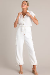 Full body view of this jumpsuit that features a collared neckline, a half button front, an adjustable self-tie waist feature, buttoned utility pockets, self-tie cuffed ankles, and folded short sleeves.