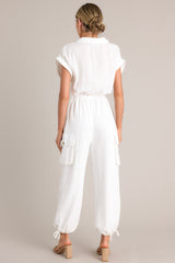 Back view of this jumpsuit that  features a collared neckline, a half button front, an adjustable self-tie waist feature, buttoned utility pockets, self-tie cuffed ankles, and folded short sleeves.