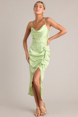 This green dress features a cowl neckline, thin adjustable crossed straps, a zipper down the back, a ruffled hip feature, and an asymmetrical hemline.