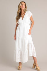 Full body view of this white maxi dress with v-neckline, removable slip, thin elastic waistband, hip pockets, eyelet detailing, and faux pearl trimmed sleeves.