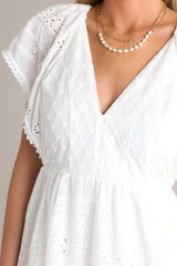 Close up view of this white maxi dress with v-neckline, removable slip, thin elastic waistband, hip pockets, eyelet detailing, and faux pearl trimmed sleeves.