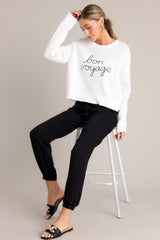 Seated angled full body view of this white sweater that features a ribbed crew neckline, embroidered wording, a soft knitted fabric, and a ribbed hemline.