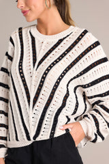 Detailed close up of the knit fabric and embroidered pattern on this loose fit, black and ecru sweater.
