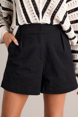 These black shorts feature a high waisted design, elastic insert in the back of the waist, hook & bar closure, an added button for extra security, a zipper, belt loops, functional hip pockets, and pleated details.