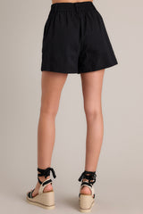 Back view of these black shorts feature a high waisted design, elastic insert in the back of the waist, hook & bar closure, an added button for extra security, a zipper, belt loops, functional hip pockets, and pleated details.