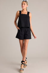 Angled full body view of this black tank that features a square neckline, thick straps that cross in the back, a relaxed fit, and an open lower back design.