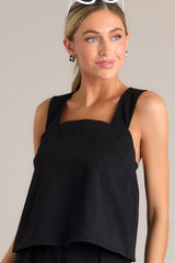 Front view of this black tank that features a square neckline, thick straps that cross in the back, a relaxed fit, and an open lower back design.