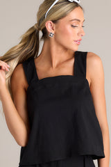 Angled front view of this black tank that features a square neckline, thick straps that cross in the back, a relaxed fit, and an open lower back design.