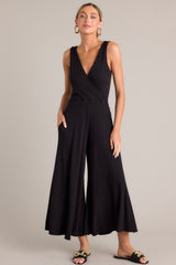 This black jumpsuit features a v-neckline, a wrap-style bodice, a fitted waist, functional hip pockets, and an extremely wide & flowing leg.
