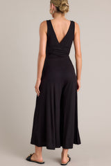 Back view of this black jumpsuit features a v-neckline, a wrap-style bodice, a fitted waist, functional hip pockets, and an extremely wide & flowing leg.