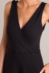 Close up view of this black jumpsuit features a v-neckline, a wrap-style bodice, a fitted waist, functional hip pockets, and an extremely wide & flowing leg.