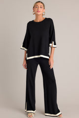 Full body view of this black sweater top that features a crew neckline, a relaxed fit, split quarter sleeves, and contrasting split hemlines.