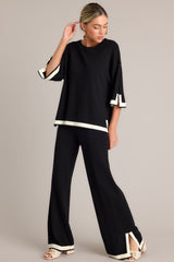 This black sweater top features a crew neckline, a relaxed fit, split quarter sleeves, and contrasting split hemlines.