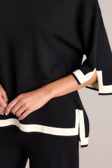 Close up view of this black sweater top that features a crew neckline, a relaxed fit, split quarter sleeves, and contrasting split hemlines.