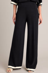 Front view of these black sweater pants that feature a high waisted design, an elastic waistband, a wide leg, and a contrasting split hemline.