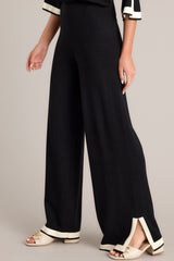 These black sweater pants feature a high waisted design, an elastic waistband, a wide leg, and a contrasting split hemline.