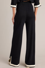 Back view of these black sweater pants that feature a high waisted design, an elastic waistband, a wide leg, and a contrasting split hemline.