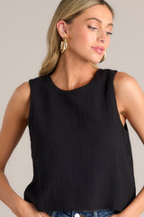 Close up view of this black top that features a crew neckline, a keyhole cutout with a functional button, and a back slit.