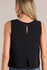 Back view of this black top that features a crew neckline, a keyhole cutout with a functional button, and a back slit.