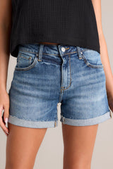 Close up front view of these cuffed denim shorts that feature a high waisted design, classic button & zipper closure, belt loops, functional front & back pockets, and a distressed cuffed hemline.