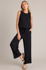 Angled full body view of these black pants that feature a high waisted design, an elastic waistband, a self-tie drawstring, functional hip pockets, and a wide leg.