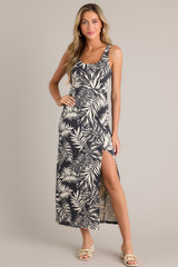 Full body view of this charcoal black midi dress that features a scoop neckline, thick straps, an elastic waistband, gathering at the hip, a side slit, and a neutral tropical print.
