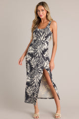 Front view of this charcoal black midi dress that features a scoop neckline, thick straps, an elastic waistband, gathering at the hip, a side slit, and a neutral tropical print.