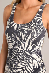 Close up view of this charcoal  black midi dress that features a scoop neckline, thick straps, an elastic waistband, gathering at the hip, a side slit, and a neutral tropical print.