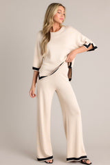 These beige sweater pants feature a high waisted design, an elastic waistband, a wide leg, and a contrasting split hemline.