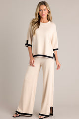 Full body view of these beige sweater pants that feature a high waisted design, an elastic waistband, a wide leg, and a contrasting split hemline.