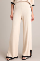 Front view of these beige sweater pants that feature a high waisted design, an elastic waistband, a wide leg, and a contrasting split hemline.