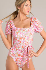 Front view of this one piece that features a square neckline, removable padding, elastic cuffed short sleeves, a removable self-tie belt, and a slightly cheeky backside. 