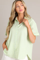 Angled front view of this light green top with collared neckline, front buttons, cuffed short sleeves, single pleat detail in back.