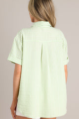 Back view of this light green top with collared neckline, front buttons, cuffed short sleeves, single pleat detail in back.