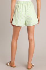 Back view of these light green high-waisted shorts with elastic insert at back waist, hook & bar closure, functional zipper, pleat detailing, hip pockets, striped pattern.