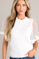 Untucked front view of this white top featuring a crew neckline, a soft stretchy fabric, and sheer short butterfly sleeves.
