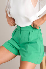 Close up angled view of these kelly green shorts that feature an elastic insert in the back of the waist, belt loops, and functional waist pockets.