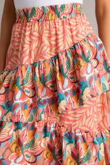 Close up view of this skirt that features an elastic waistband, tiered ruffles, colorful prints, and an asymmetrical hem.