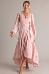 Front view of this pink wrap dress that features a v-neckline, balloon sleeves, an adjustable tie around the waist, and an asymmetrical flowy skirt.