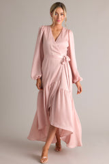 Full body view of this dusty pink wrap dress featuring a v-neckline, balloon sleeves, an adjustable tie around the waist, and an asymmetrical flowy skirt.