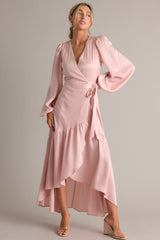 This dusty pink wrap dress features a v-neckline, balloon sleeves, an adjustable tie around the waist, and an asymmetrical flowy skirt.